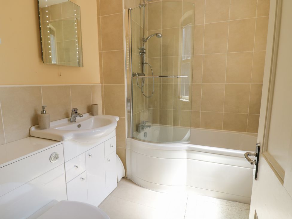 A bathroom with a sink vanity unit mirror and a bathtub with glass shower screen at Angorfa in Llanbedr