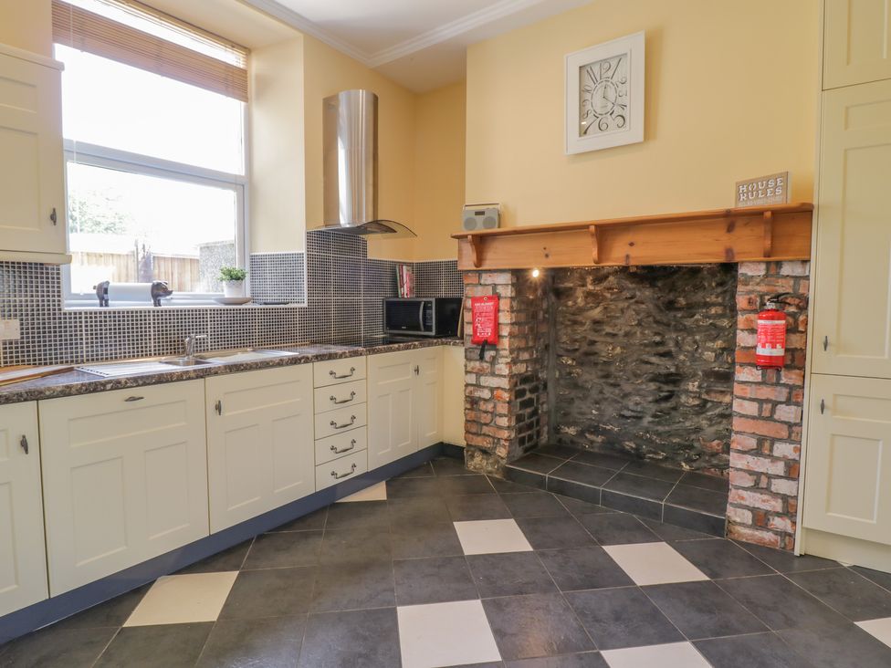 A kitchen with white cabinets a window above the sink a microwave and an exposed brick fireplace at Angorfa in Llanbedr
