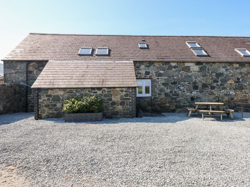 A stone building with a small bush in a planter and a wooden picnic table on a gravel ground at Hafod in Pontllyfni