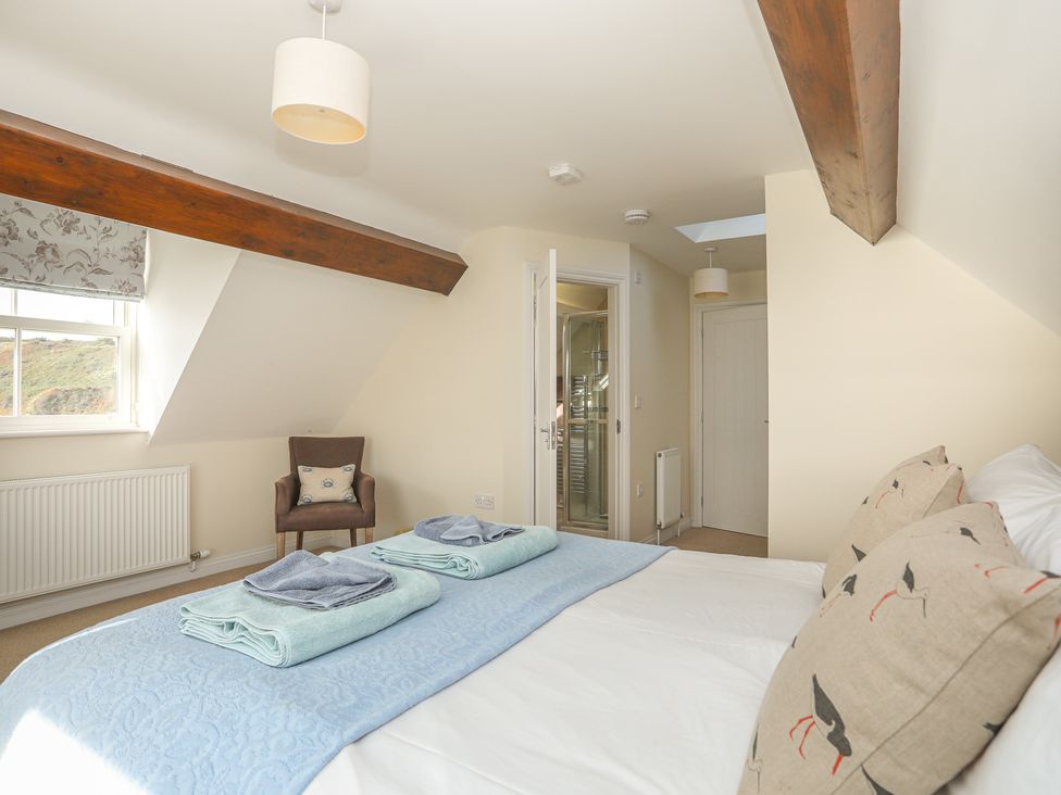 A bedroom with a bed folded towels and an armchair near a window at The Old Lifeboat House in Penmon