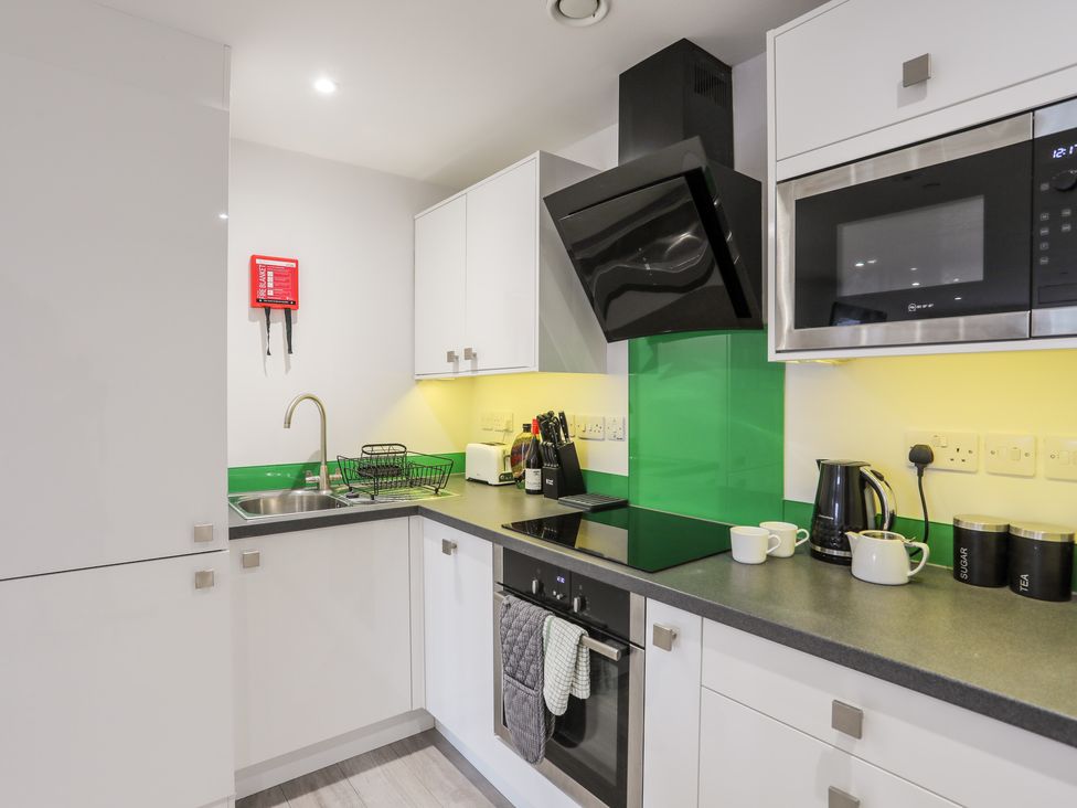 A kitchen with white cabinets a sink stovetop microwave kettle and containers at Sea Breeze Benllech