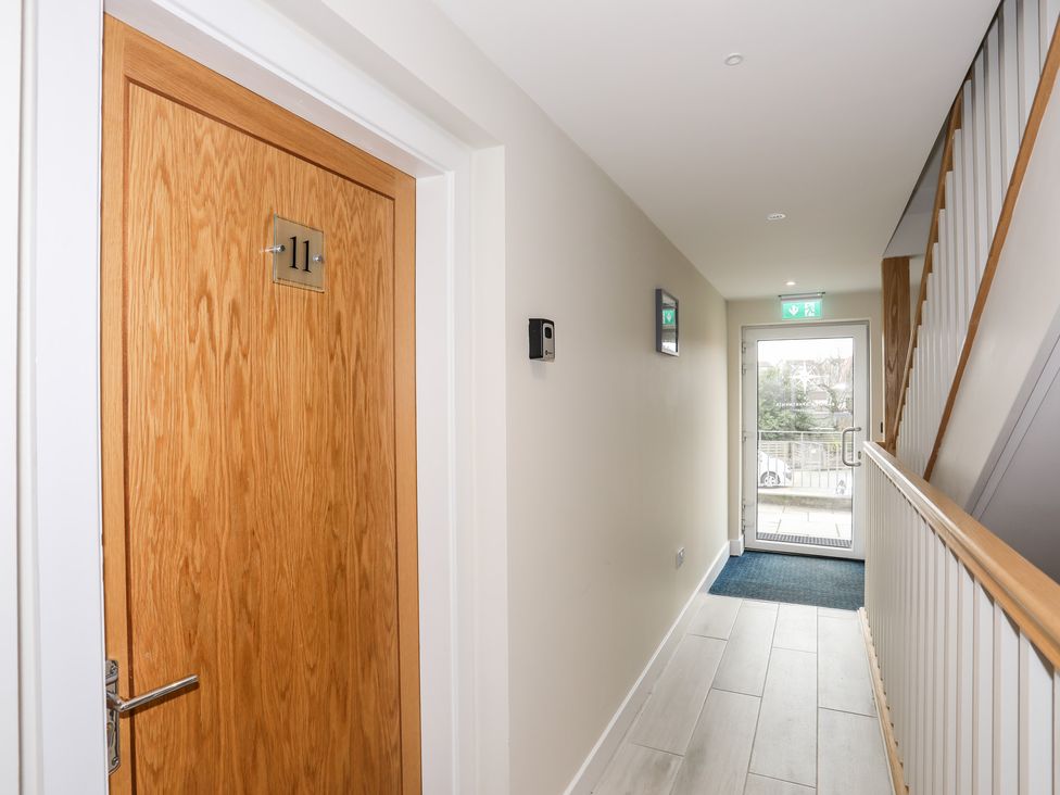 A hallway with a wooden door numbered 11 a stair railing and a glass exit door with an exit sign at Sea Breeze in Benllech