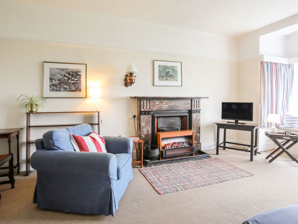 A living room with a blue armchair red and white striped cushion fireplace and television at Windygates in Rhosneigr