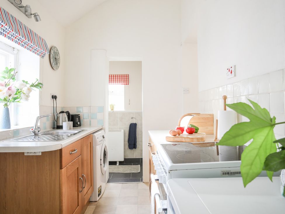 A kitchen with a sink countertop washing machine stove and cutting board with vegetables at Windygates in Rhosneigr