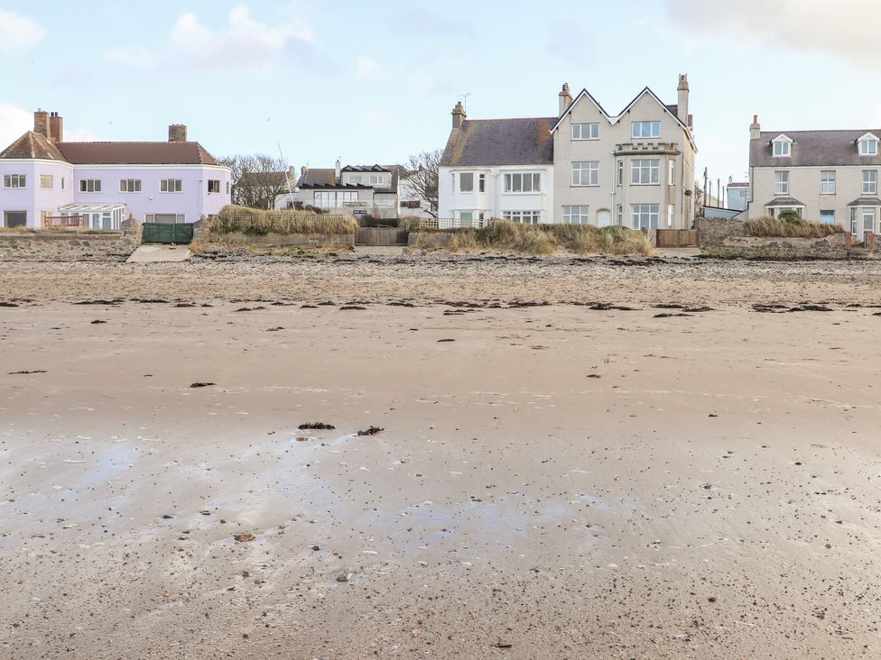 A sandy beach with seaweed patches in front of residential houses at Windygates in Rhosneigr