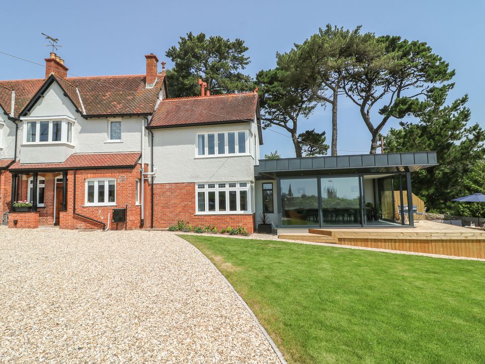 A house with a gravel driveway and a lawn with trees behind at The Coach House in Teignmouth