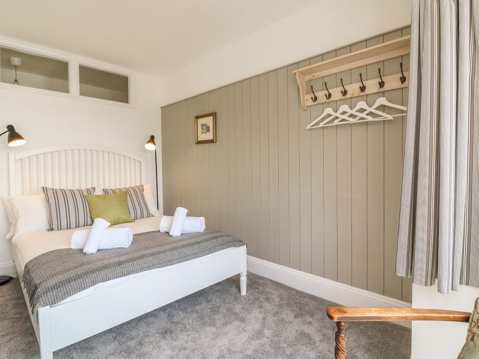 A bedroom with a bed with pillows and towels next to a wall with hangers and a chair at The Coach House in Teignmouth