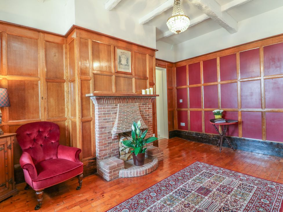 A room with wood paneling a brick fireplace a red armchair a small table with a plant and a patterned rug at The Coach House in Teignmouth
