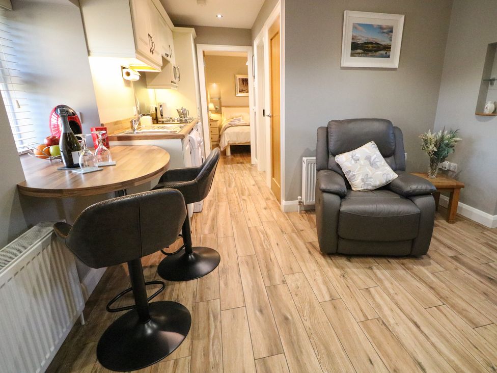 A small kitchen and seating area with bar stools and a gray armchair at Lough Island Reavy Cottage Kilcoo Mourne Mountains Newry County Down