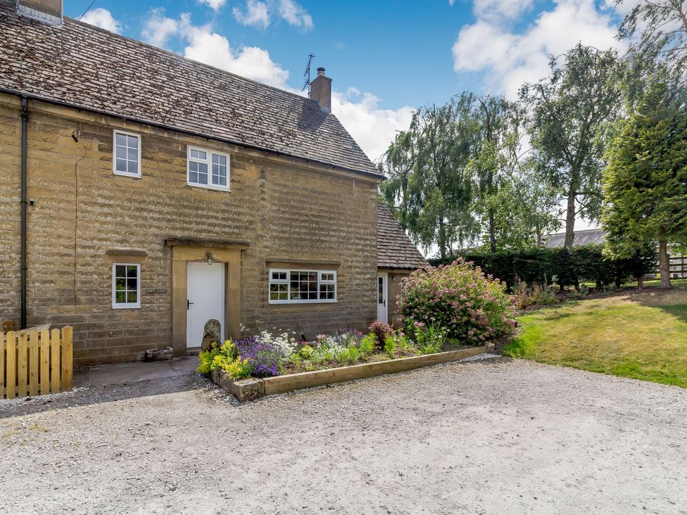 A stone house with a gravel driveway and flower beds surrounded by trees at Ivet Lowe in Hopton near Wirksworth