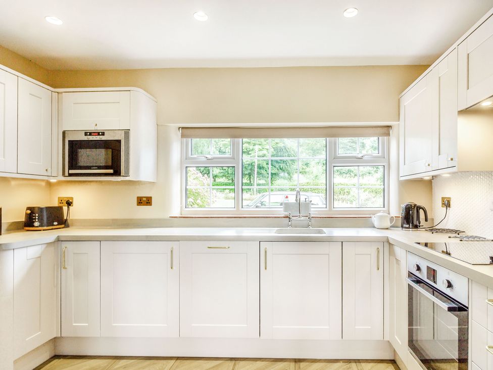 A kitchen with white cabinets a microwave a toaster a kettle an oven and a window overlooking greenery at Ivet Lowe in Hopton near Wirksworth