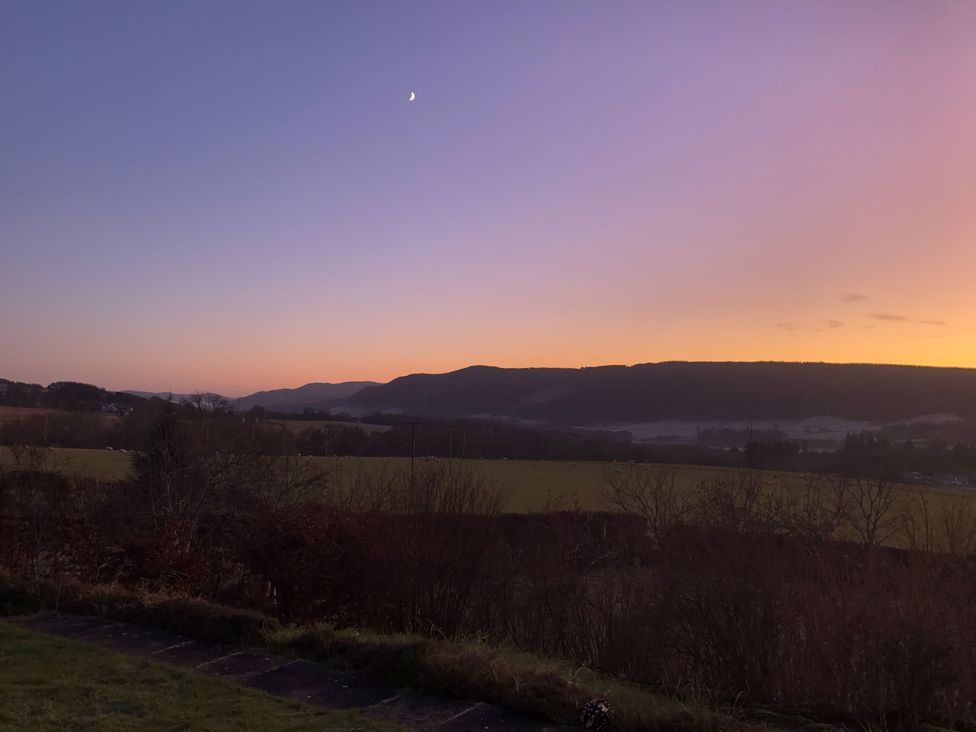 A landscape view of fields bushes and hills under a crescent moon at sunset at Balvaig in Pitlochry