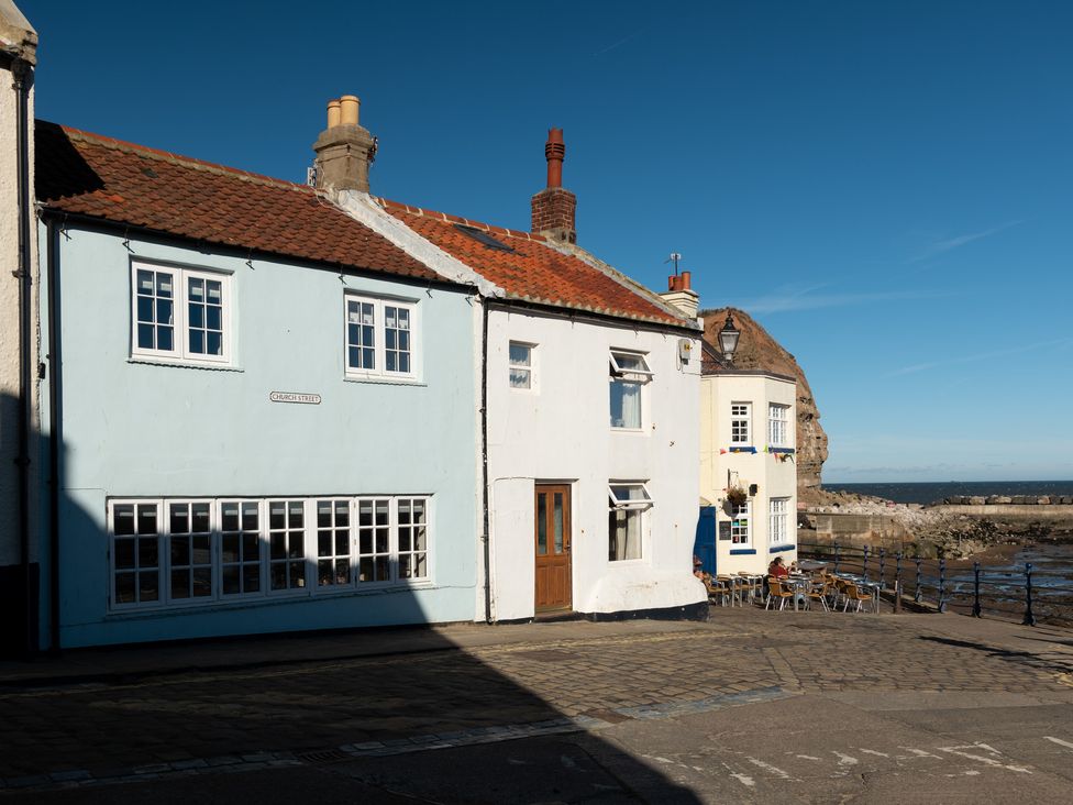 Exterior view of buildings along a cobblestone street by the sea with tables and chairs outside at Roxby Cottage in Staithes
