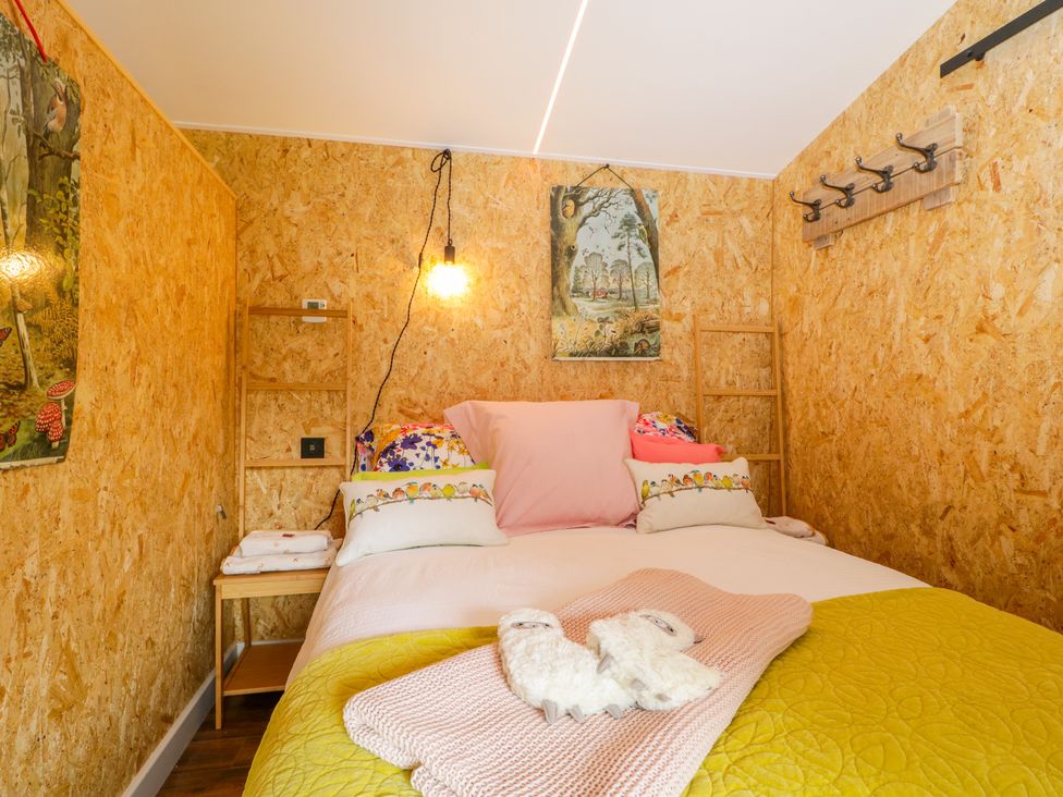 A small bedroom with a double bed pillows and blankets on the bed a bedside table and wall hooks at The Chard in Longtown