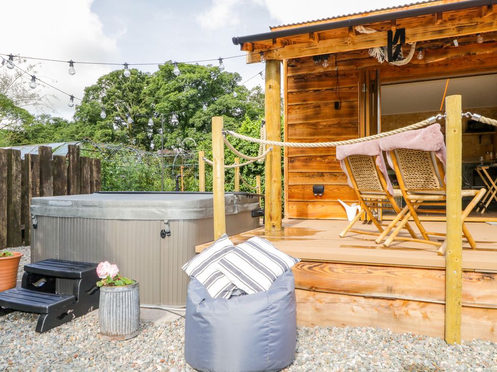 An outdoor area with a hot tub bean bag chair with pillows wooden deck with chairs and string lights at The Chard in Longtown