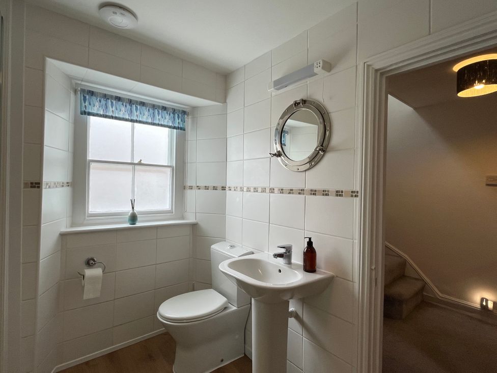 A bathroom with a toilet a sink and a round mirror next to a window at The Ferryman in Weymouth