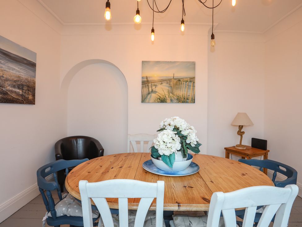 A dining room with a round wooden table and mixed chairs a flower centerpiece and paintings on the walls at Casita in Benllech