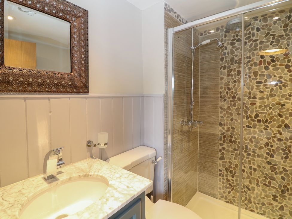 A bathroom with a sink and faucet a toilet and a shower with pebble tile walls at Rosebank Cottage in Mortehoe
