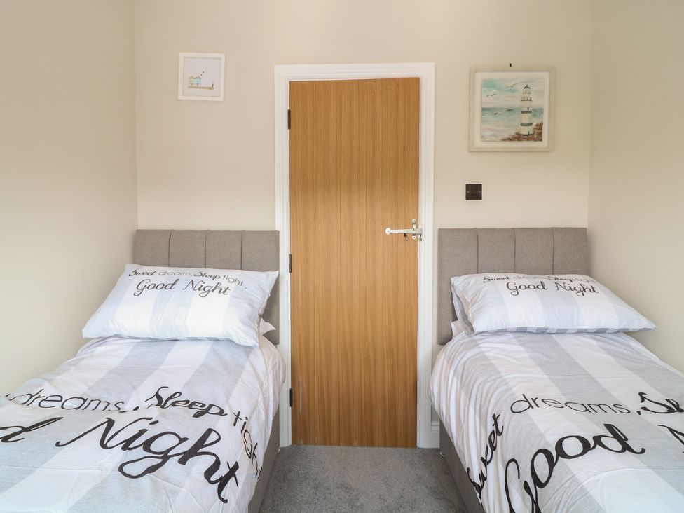 A bedroom with two single beds with grey headboards and light bedding with text in front of a wooden door at Rosebank Cottage in Mortehoe
