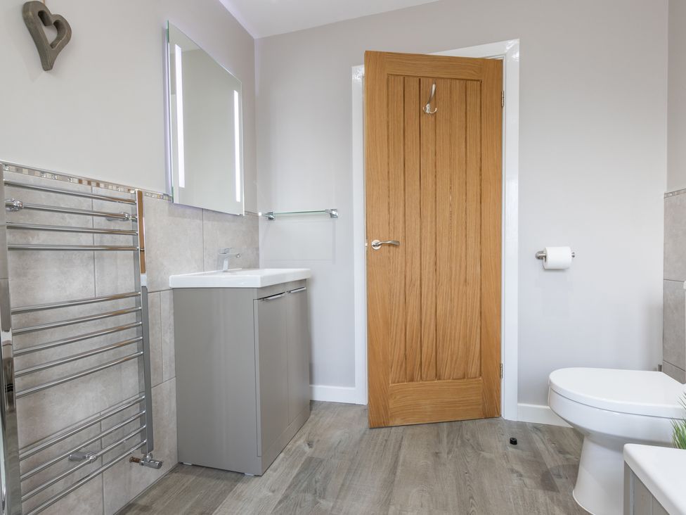 A bathroom with a wooden door a gray sink cabinet a toilet and a heated towel rail at Cartref in Trawsfynydd