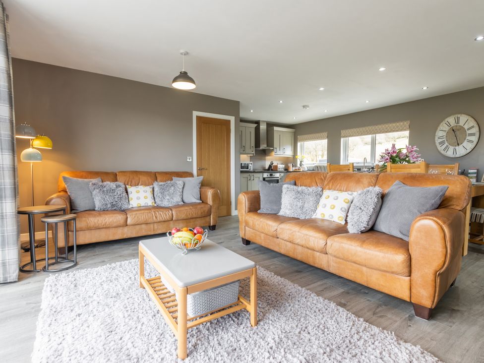 A living room with two leather sofas a coffee table with fruit and a kitchen area at Cartref in Trawsfynydd