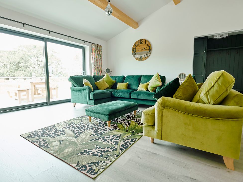 A living room with green and yellow sofas a patterned rug a wooden clock on the wall and large glass doors at Whernside Lodge in Rathmell near Settle