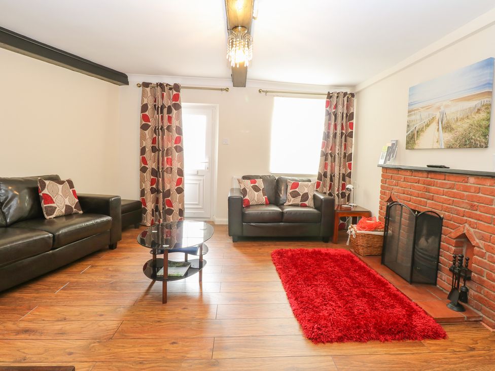 A living room with two black leather sofas a glass coffee table a red rug and a brick fireplace at Compass Cottage in Bodham near Sheringham