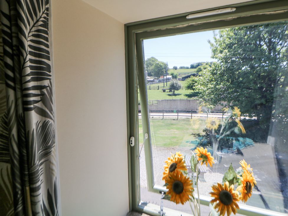 A window with sunflowers in front and a view of a green field and trees at Meadow View in Buxton