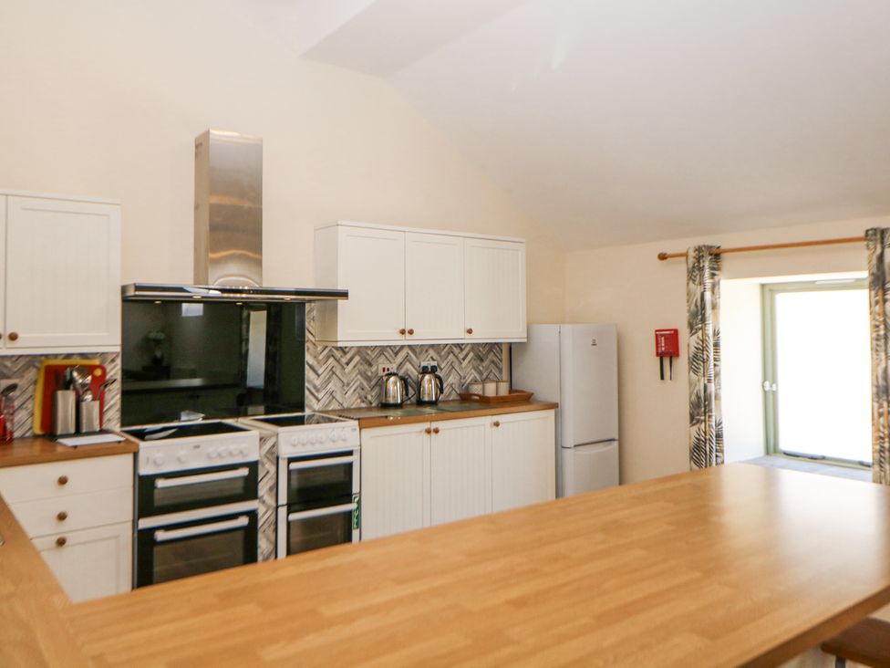 A kitchen with white cabinets wooden countertops two ovens a refrigerator and a window with patterned curtains at Meadow View in Buxton