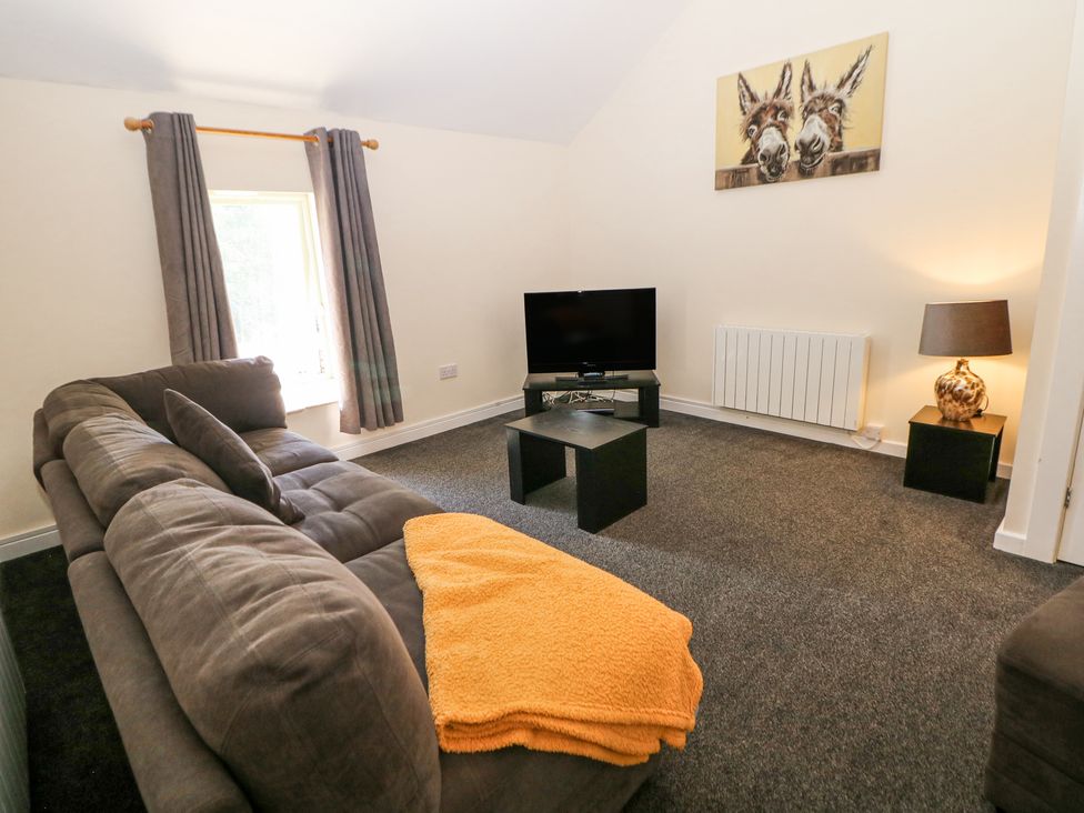 A living room with a gray couch orange blanket small black tables a TV and a painting of two donkeys at Meadow View in Buxton