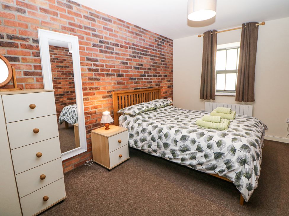A bedroom with a bed covered in leaf patterned bedding a bedside table with a lamp a tall chest of drawers a floor mirror and a window with curtains at Meadow View Buxton