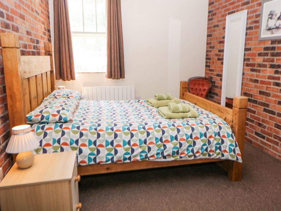 A bedroom with a wooden bed frame patterned bedding green towels bedside table lamp armchair and full length mirror at Meadow View in Buxton