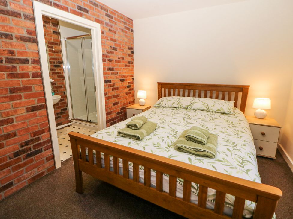 A bedroom with a wooden bed and leaf patterned bedding two bedside tables with lamps and a door leading to a bathroom with a shower at Meadow View in Buxton