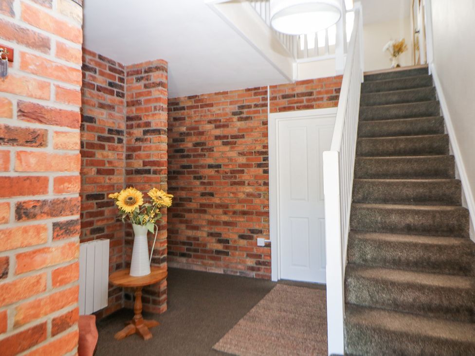 A hallway with a carpeted staircase a small wooden table with a vase of flowers and exposed brick walls at Meadow View in Buxton