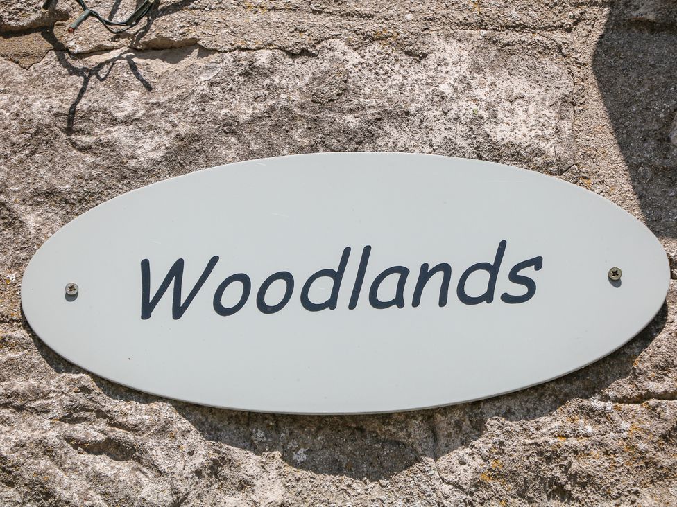A white oval sign with the word Woodlands mounted on a stone wall at Meadow View in Buxton