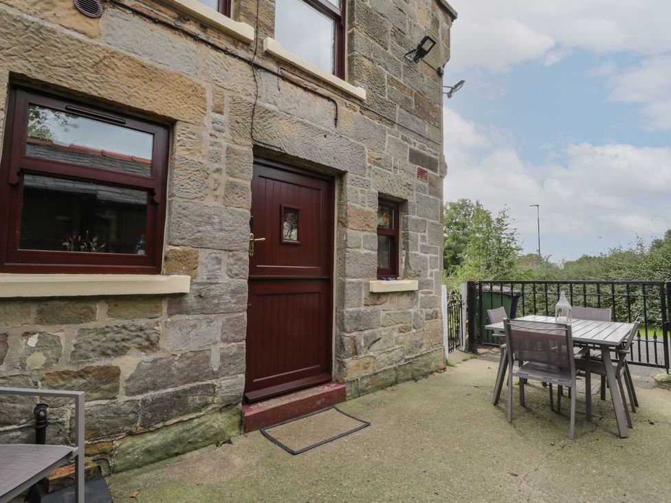 A stone exterior wall with a wooden door and windows next to a patio area with a table and four chairs at Foulsyke Farm Cottage in Loftus