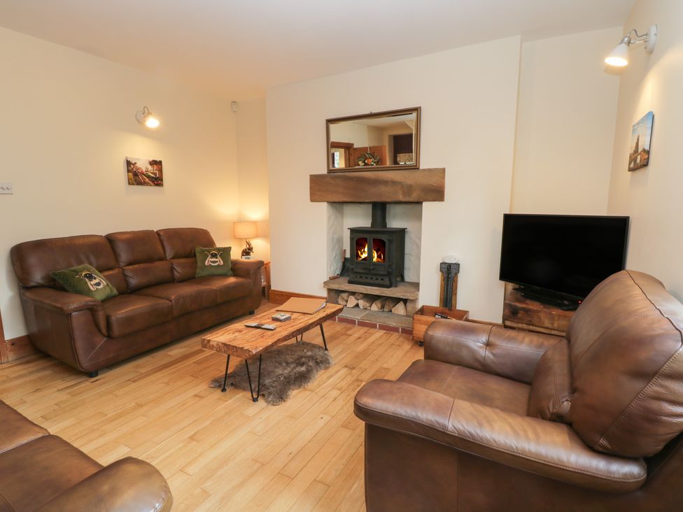 A living room with leather sofas a wood burning stove and a television at Foulsyke Farm Cottage in Loftus