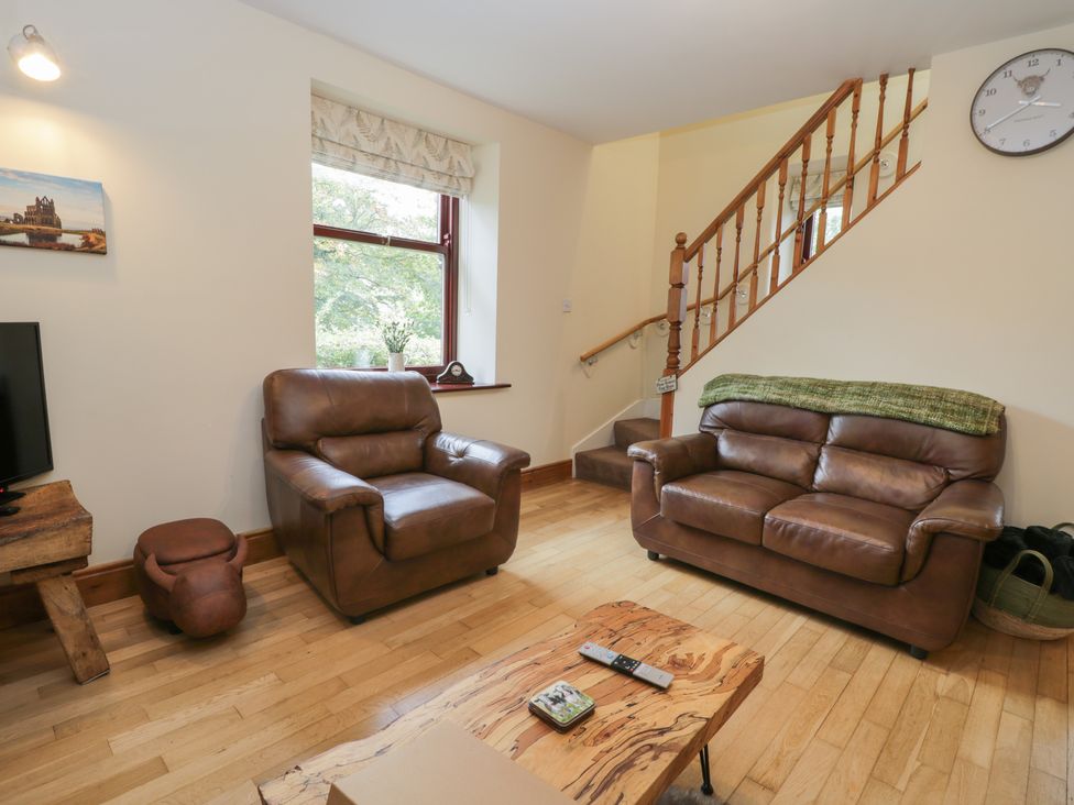 A living room with brown leather armchairs a wooden table and a staircase at Foulsyke Farm Cottage in Loftus