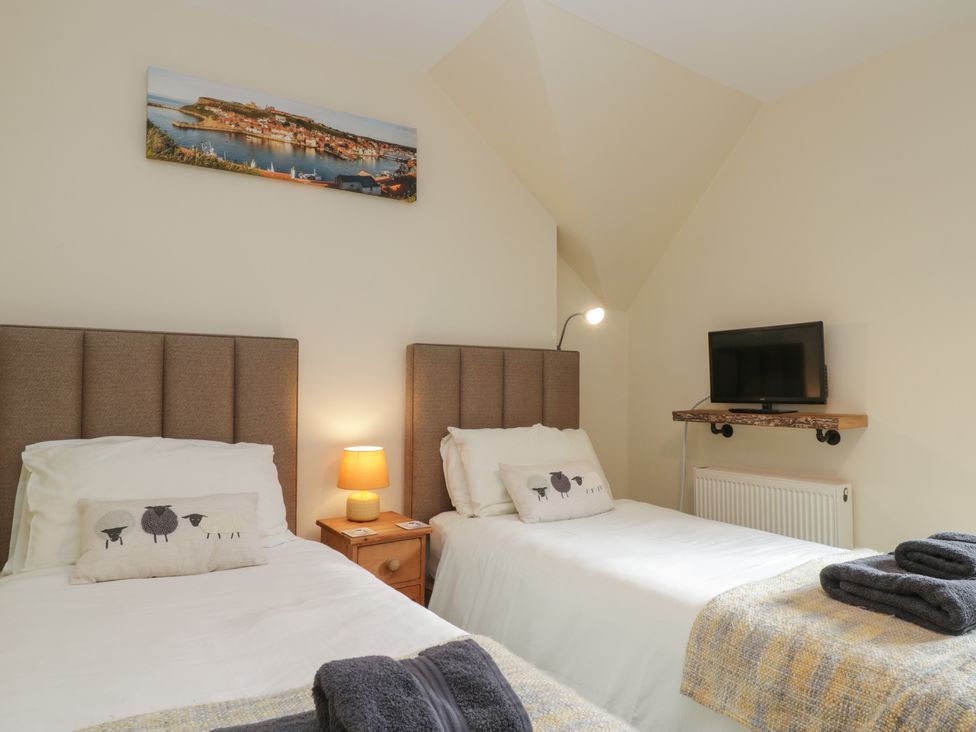 A bedroom with two single beds side by side a small wooden bedside table with a lamp a wall-mounted TV and a framed picture above the beds at Foulsyke Farm Cottage Loftus