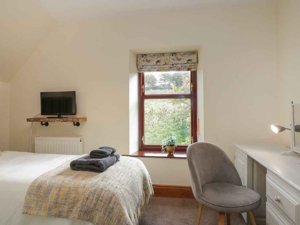 A bedroom with a bed folded towels on top a window with a plant a grey chair and a white desk with a lamp at Foulsyke Farm Cottage in Loftus