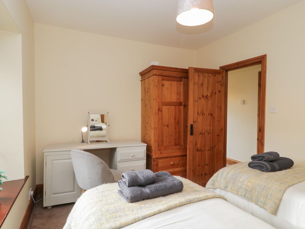 A bedroom with two single beds, a wooden wardrobe, a white desk, and a grey chair at Foulsyke Farm Cottage in Loftus