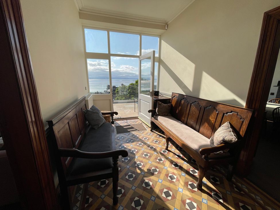 A hallway with two wooden benches and a door leading to a balcony with a view at Victoria Mount in Grange-Over-Sands