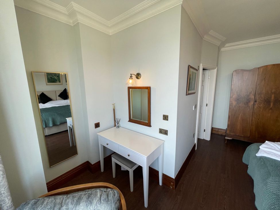 A bedroom with a white dressing table and mirror next to a tall mirror and a wooden wardrobe at Victoria Mount in Grange-Over-Sands