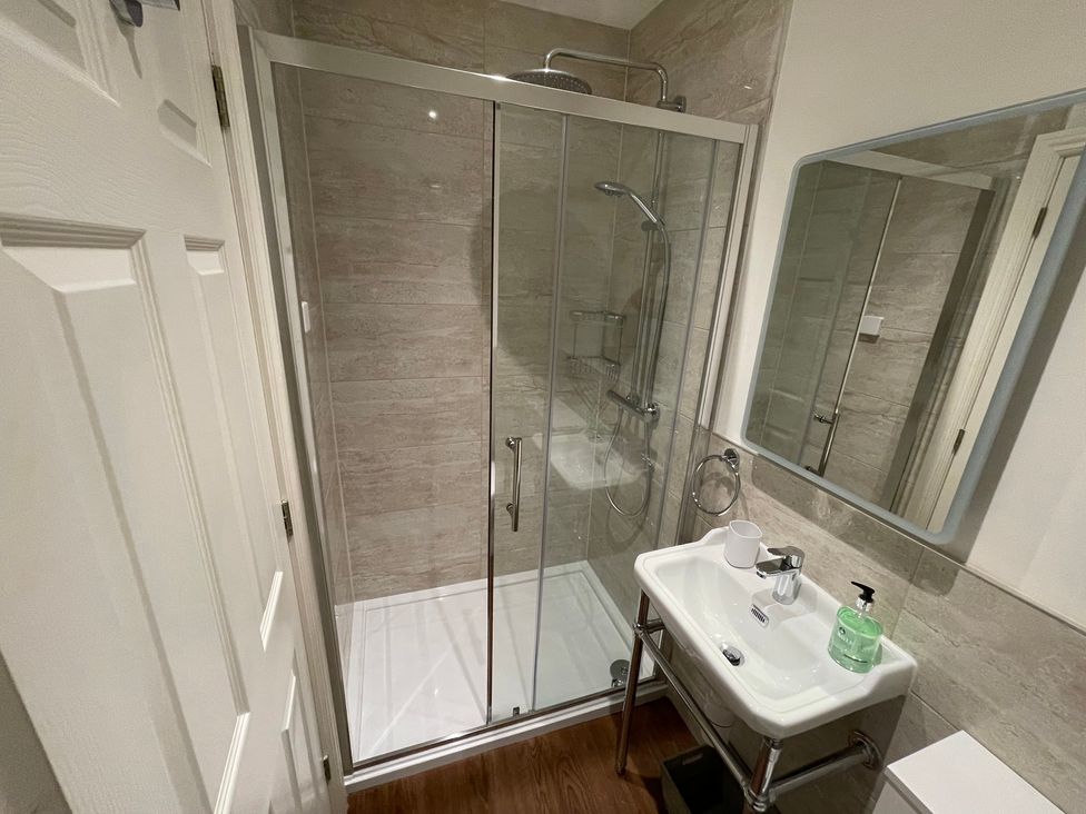 A bathroom with a glass shower enclosure a sink with a mirror above it and a soap dispenser at Victoria Mount in Grange-Over-Sands