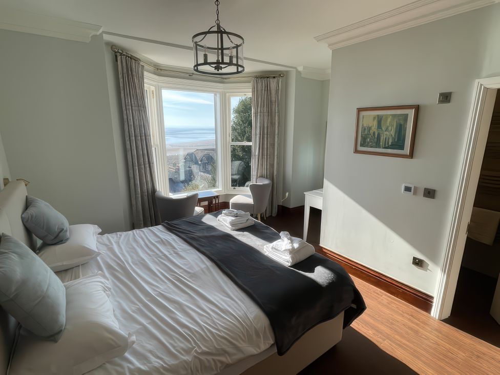 A bedroom with a bed two chairs and a table by a bay window at Victoria Mount in Grange-Over-Sands