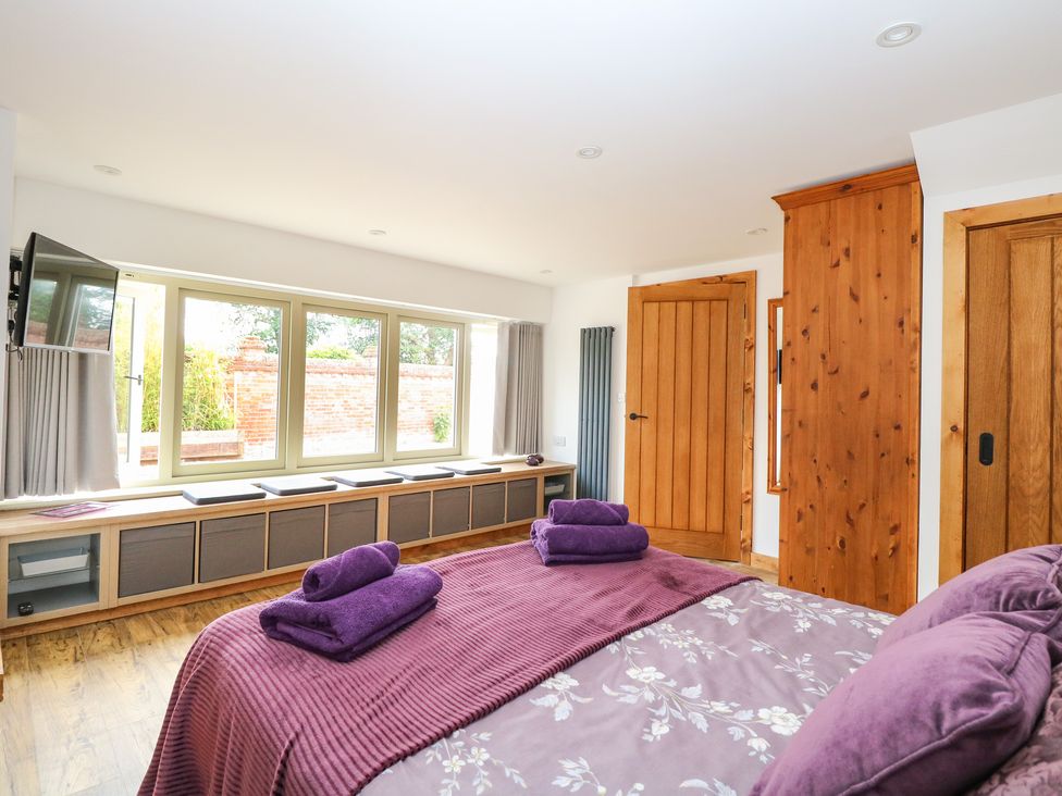 A bedroom with purple bedding and towels a wooden bench under windows and wooden doors at Cobblers Barn in Repps With Bastwick near Potter Heigham