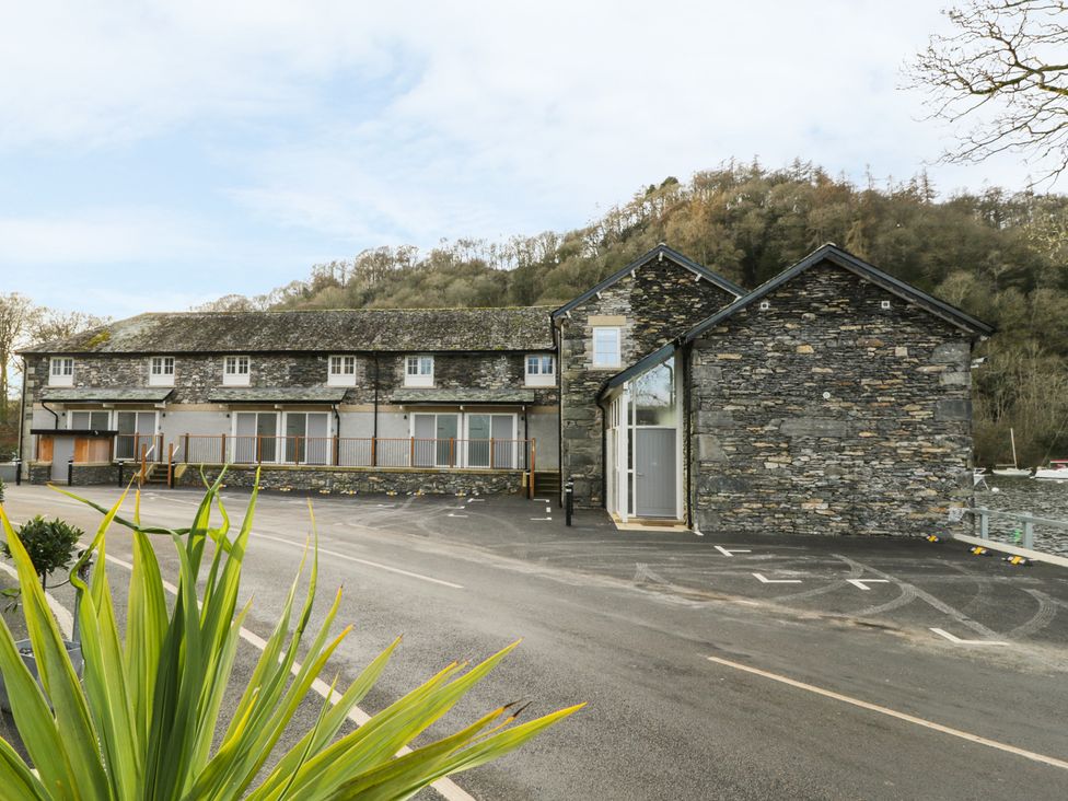 Exterior view of a stone building with multiple windows and parking spaces near a wooded hill at Pennington in Far Sawrey