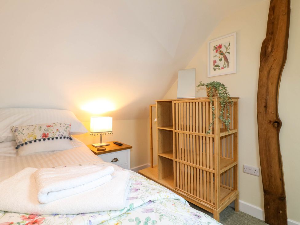 A bedroom with a bed pillow and folded towels on the bed next to a wooden cabinet with a plant and framed picture at The Long Barn in Alton