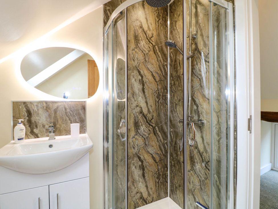 A bathroom with a sink cabinet and a glass shower enclosure with marbled wall panels at The Long Barn in Alton