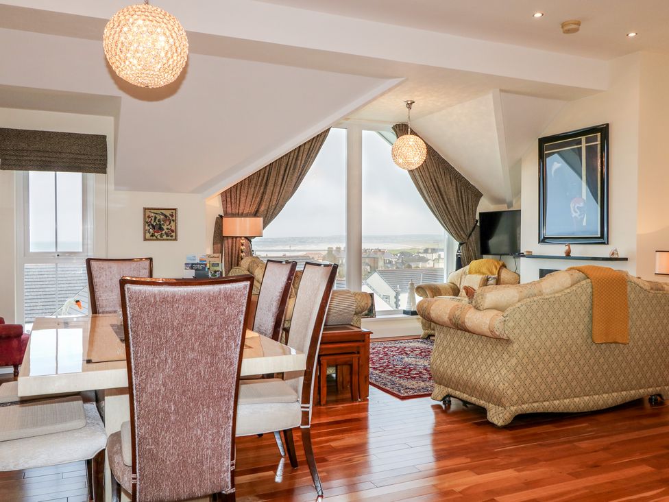 A dining area with six chairs and a living room with two sofas and a TV by large windows at Seaview in Castlerock